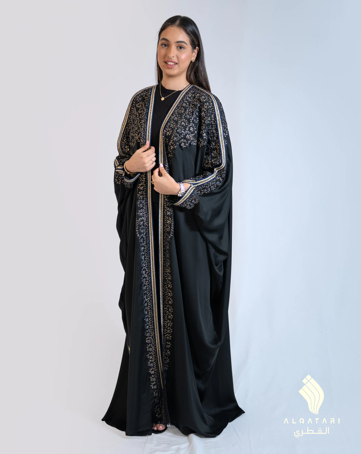 Model wearing a black Bahraini abaya with intricate hand and machine embroidery in gold and blue tones, designed for formal occasions and weddings. Abaya from Al Qatari Gallery collection