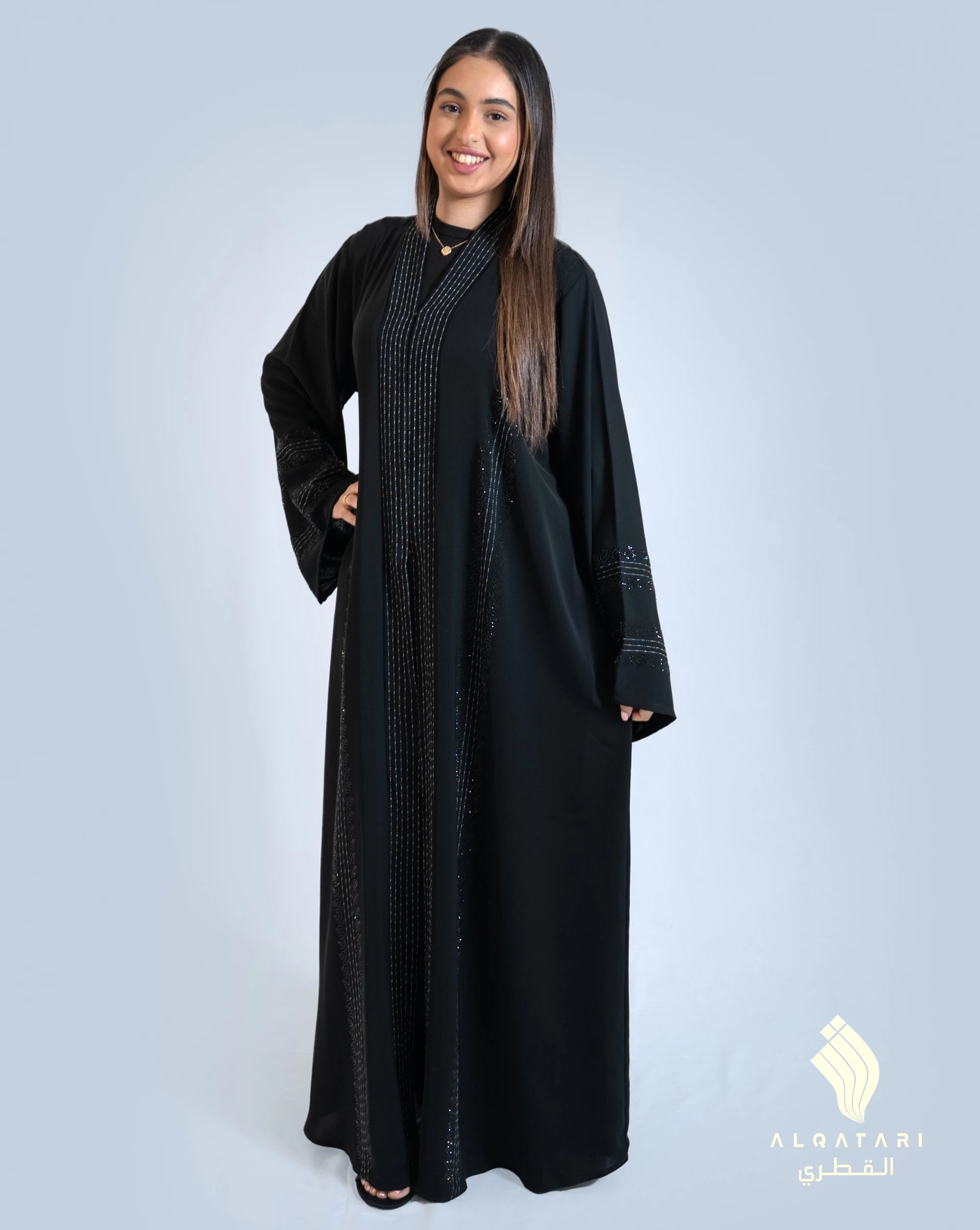 Front view of a woman wearing an elegant black abaya with contrast stitch lines and bead-embroidered details, designed from breathable Nada fabric. Abaya from Al Qatari Gallery Collection