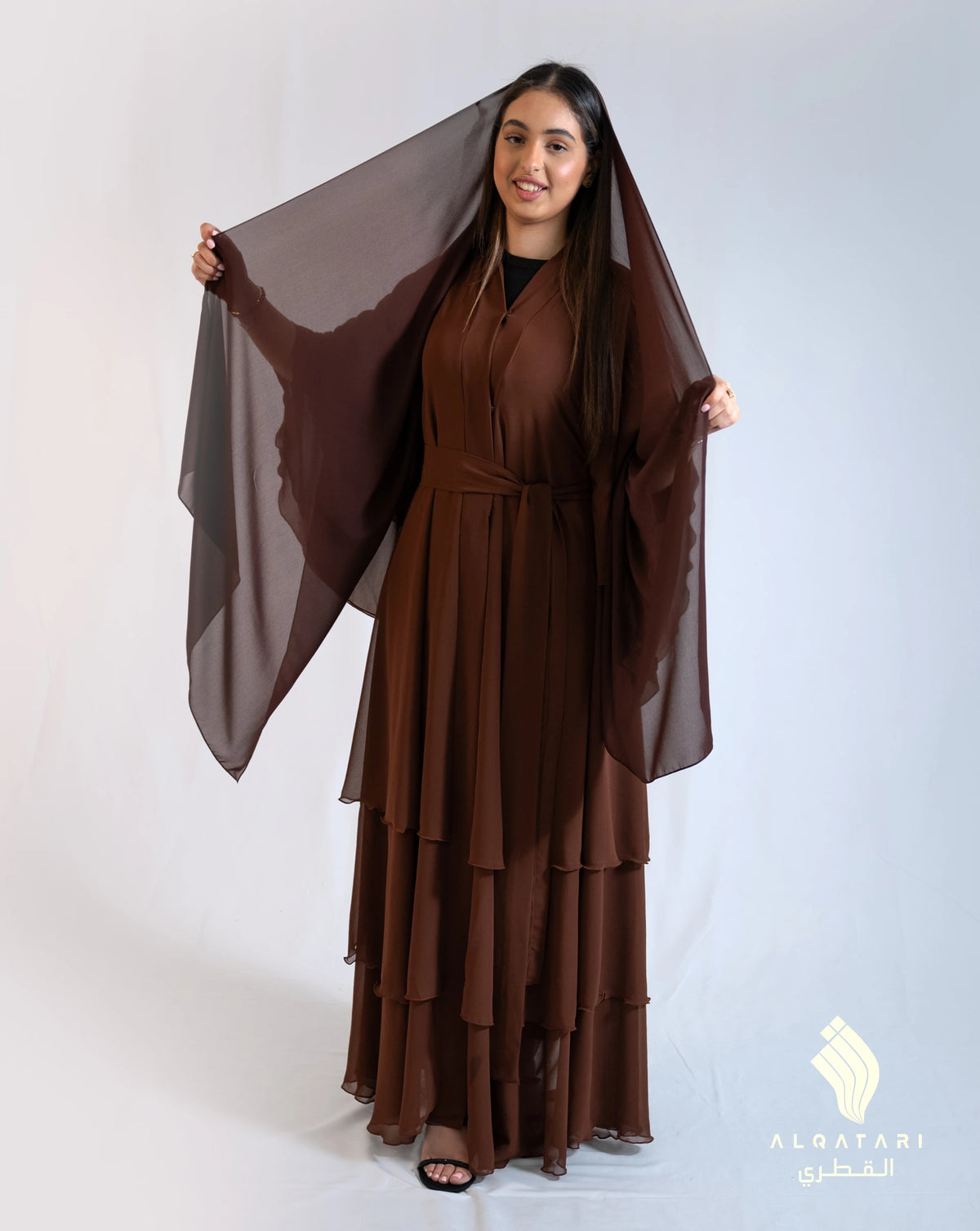 Woman wearing a flowing chocolate-coloured chiffon frill abaya with layered ruffles and a sheer matching scarf. Modest and elegant abaya, ideal for spring wear from Al Qatari Gallery