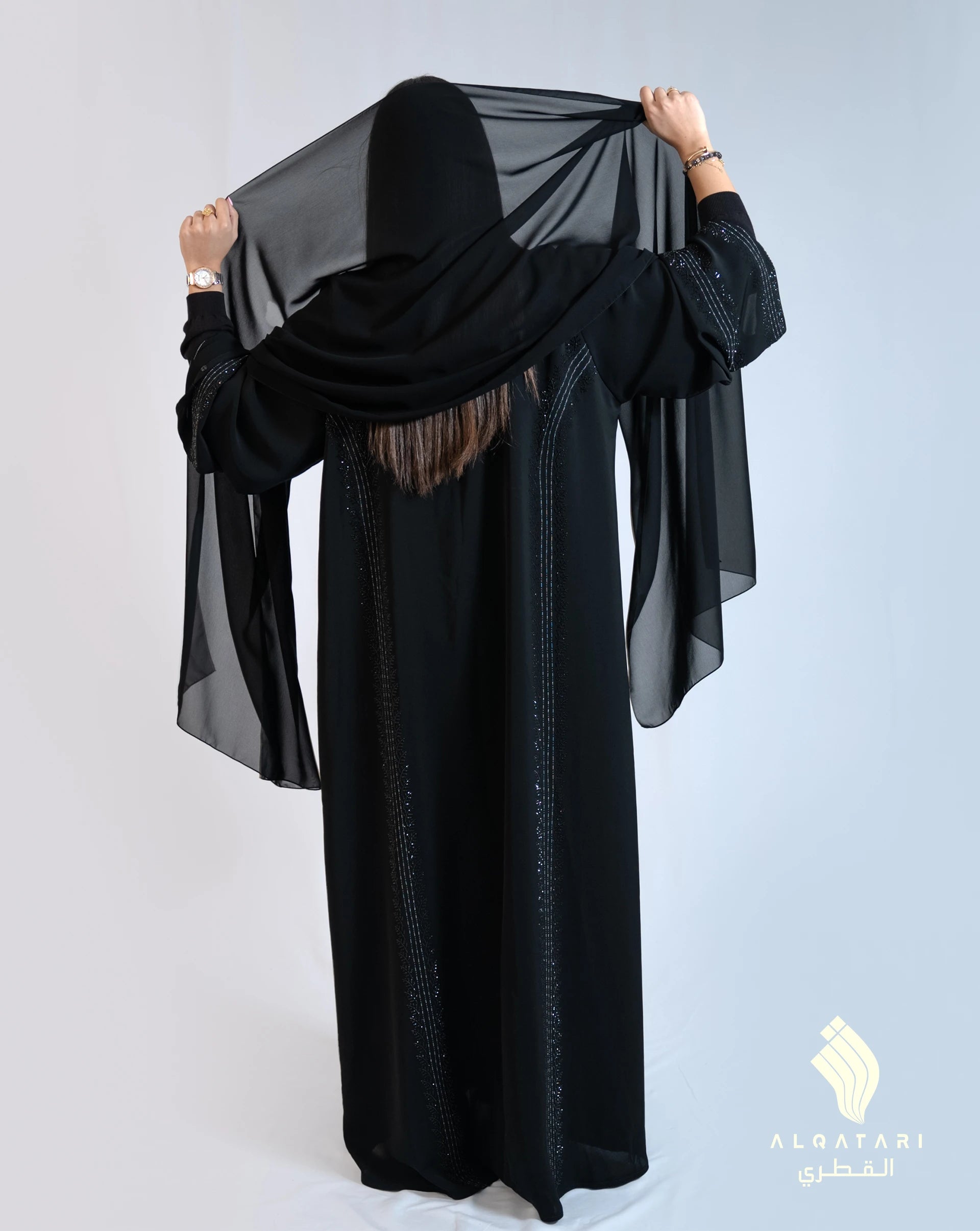 Back view of the black abaya showing vertical beadwork details and a sheer black chiffon sheila draped over the model’s head and shoulders. Abaya from Al Qatari Gallery collection