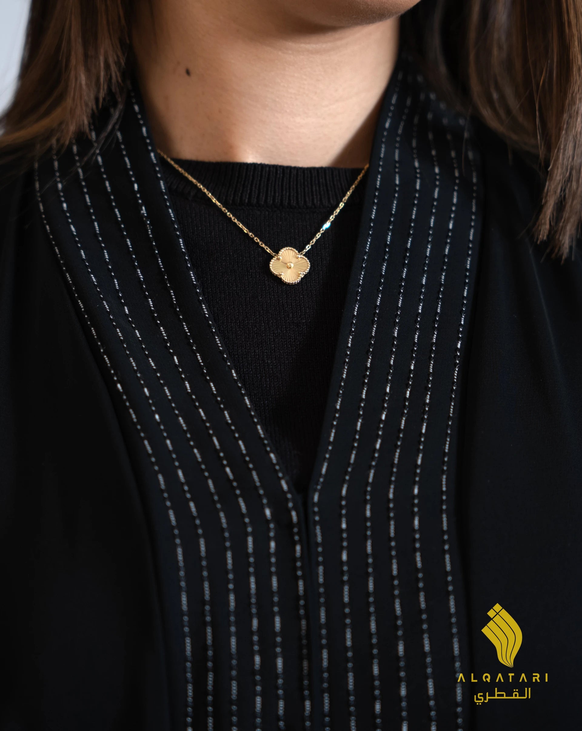 Close-up view showing fine contrast stitching and beaded embroidery on the neckline of a black abaya, worn with a gold pendant necklace. Abaya from Al Qatari Gallery
