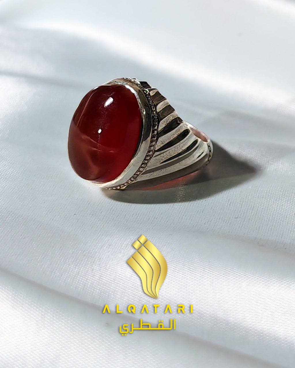 Side view of a silver men’s ring with a polished red Yemeni Aqeeq stone by Alqatari on a white fabric background