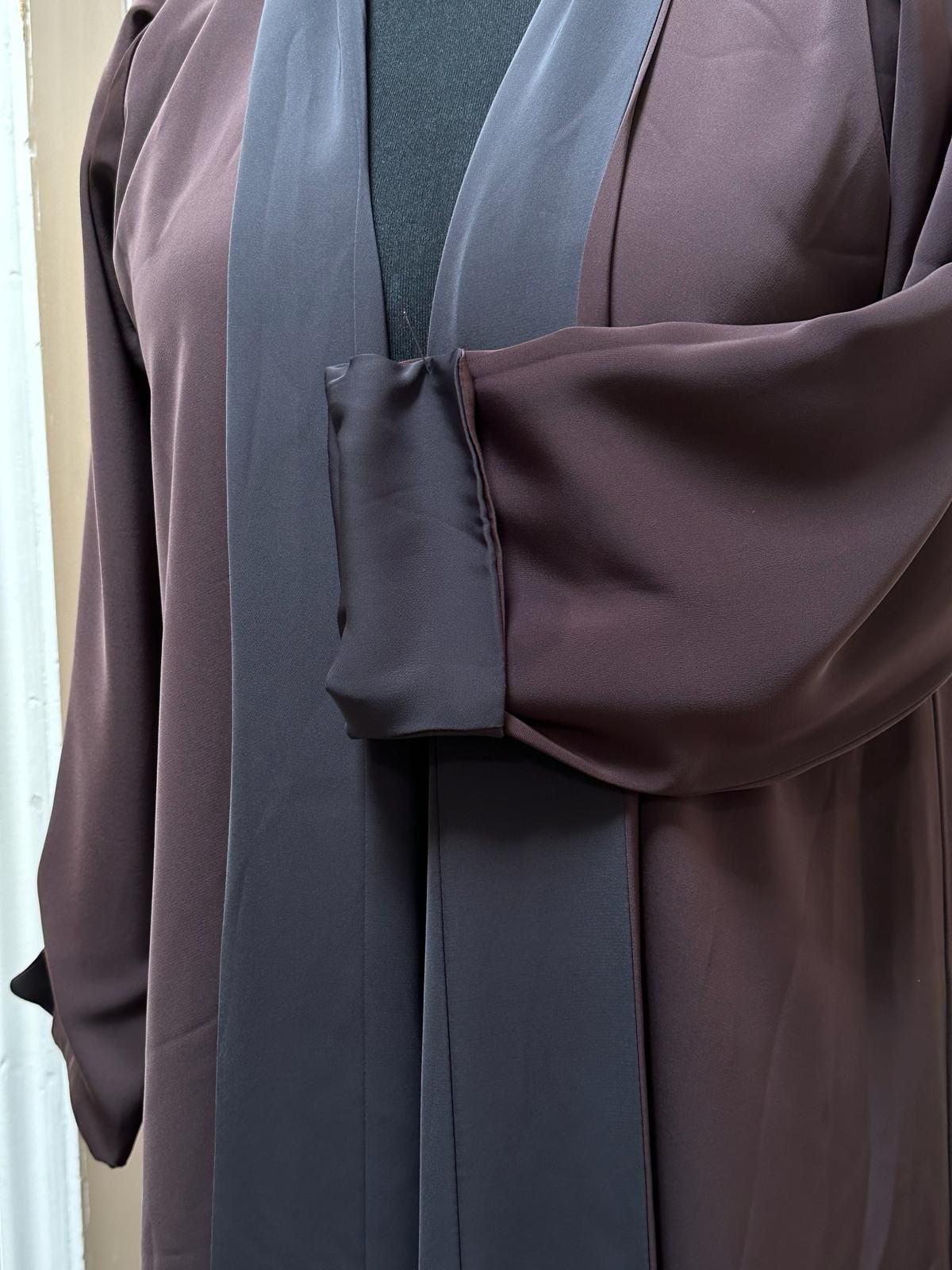Dark brown and grey two-toned abaya from Al Qatari Gallery shown on mannequin, highlighting sleeve cuff design and front trim.