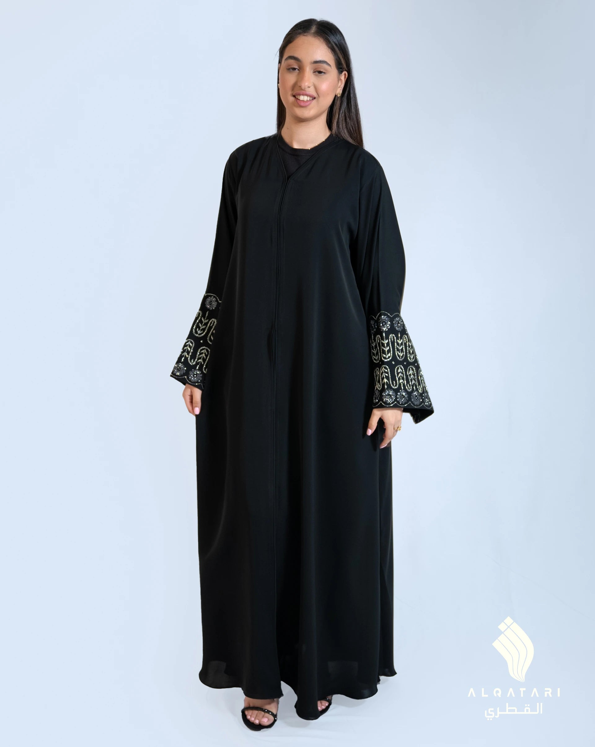 Model wearing a lush black flowy abaya from the Al Qatari Gallery collection, featuring silver and charcoal embellished sleeves in an elegant Nada fabric – sizes 54, 56, 58.