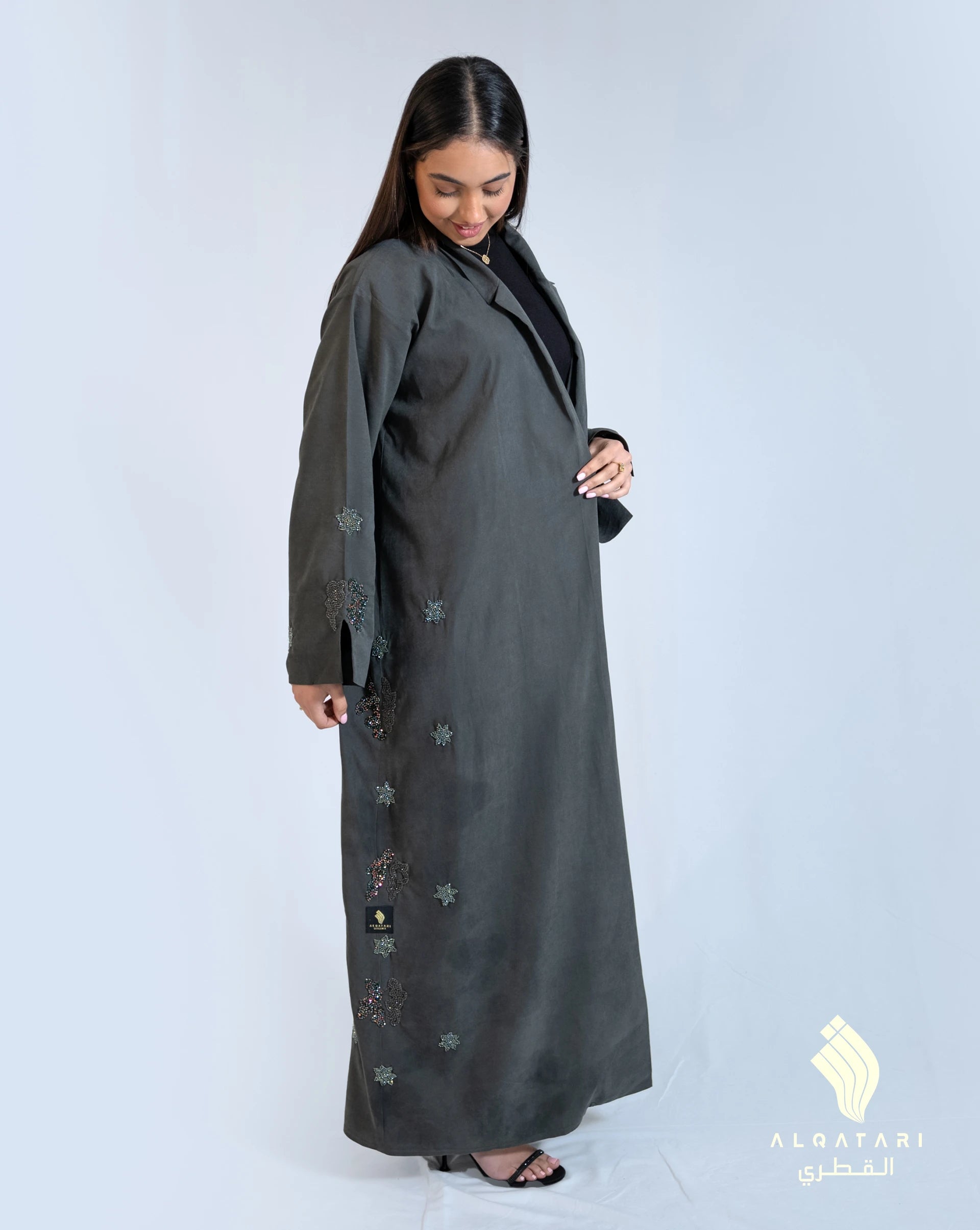 Woman wearing a collared suede abaya from Al Qatari Gallery in bottle green, embellished with hand-applied beads along the side for a refined, modest fashion look. 