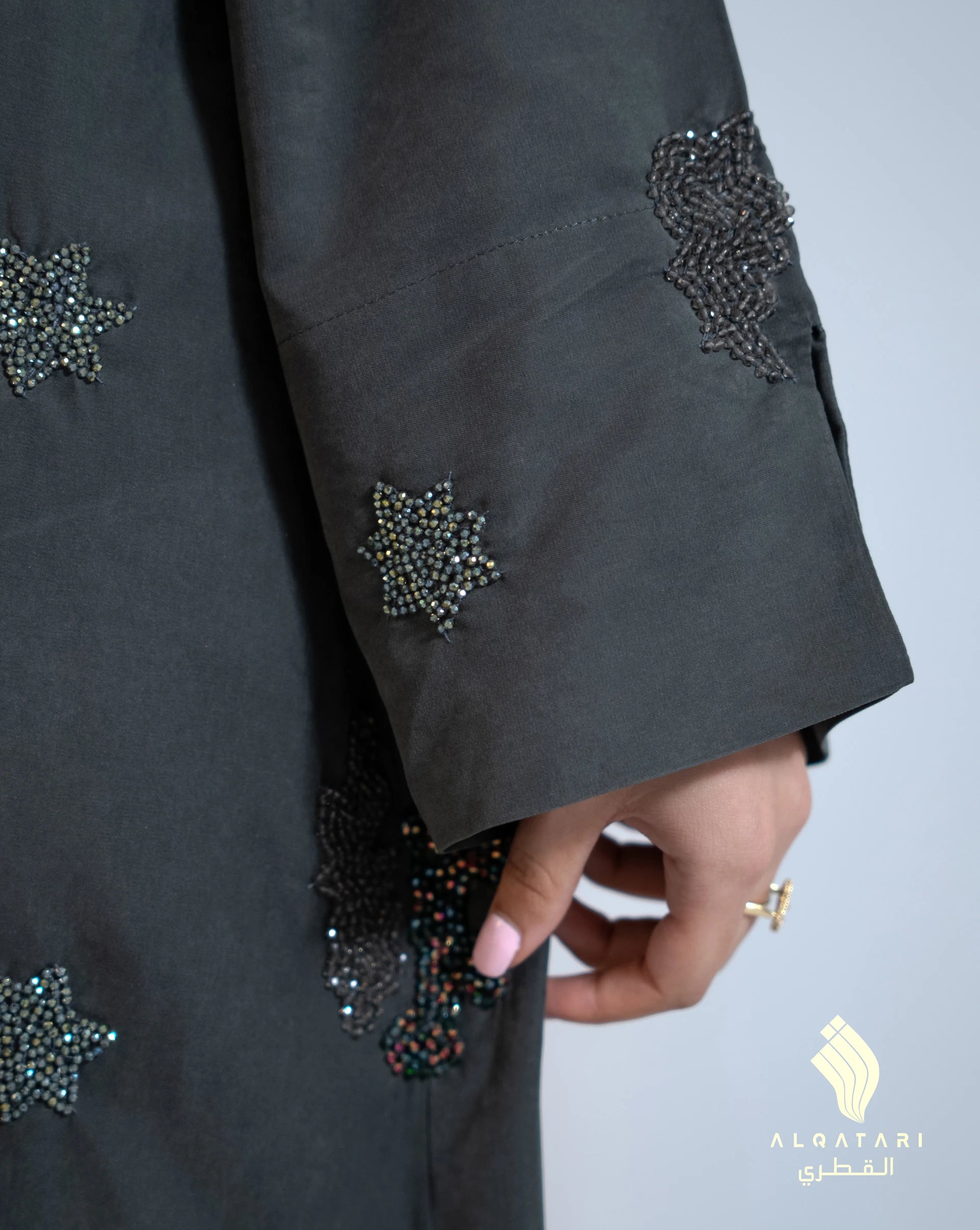 Close-up of the sleeve of the suede abaya from Al Qatari Gallery, showing fine star-shaped bead embroidery and glossy texture of the fabric. 