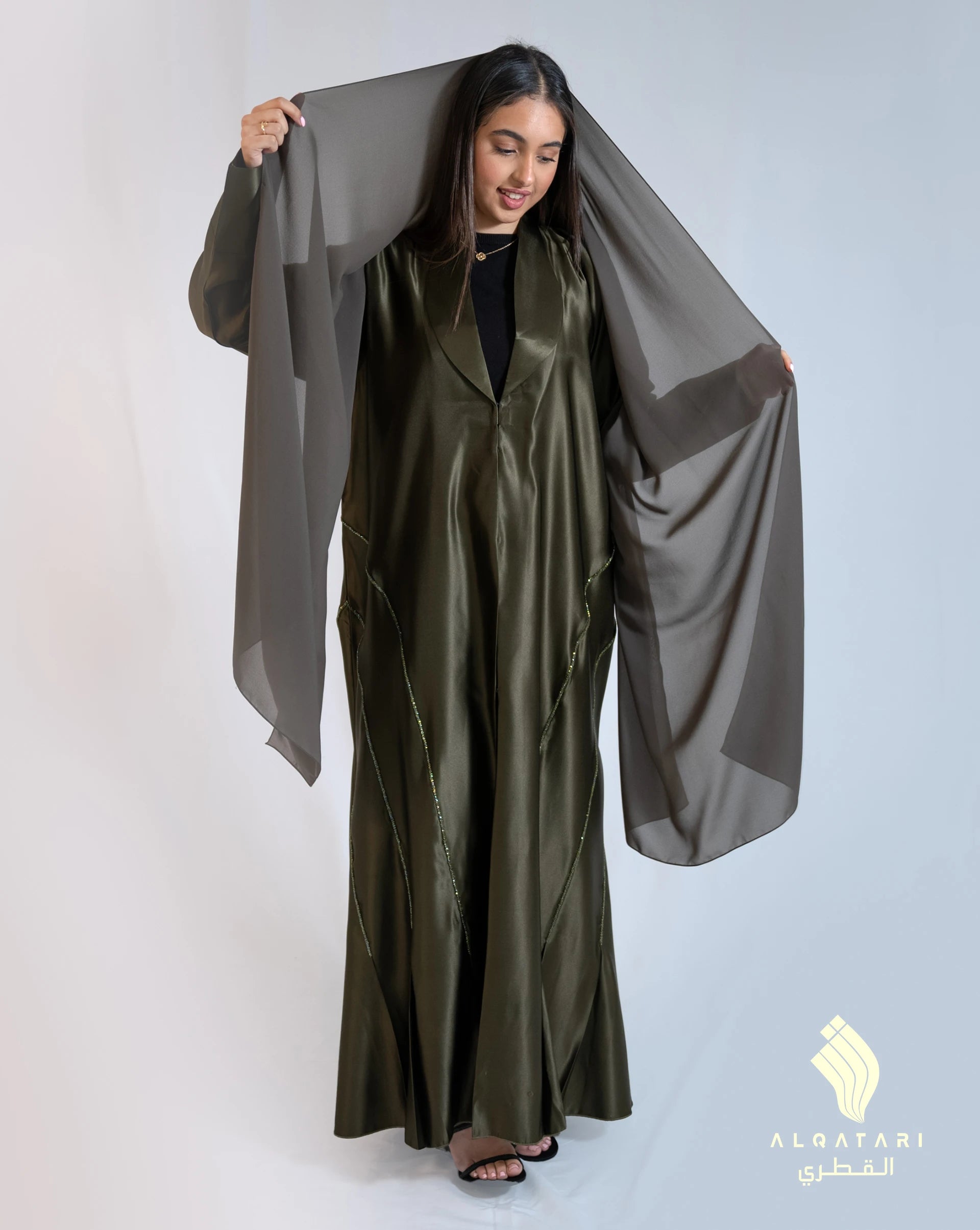 Model wearing a khaki green satin abaya with handwork from the Al Qatari Gallery collection – elegant evening modest wear in size 56.