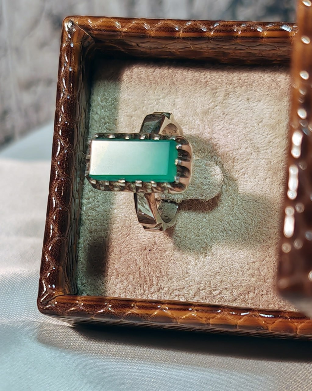 Top view of rectangular green gemstone ring in a velvet-lined brown ring box by Al Qatari Gallery Rings Jewellery