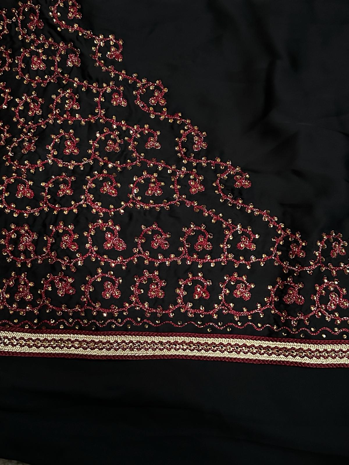 Close-up of detailed red and gold embroidery on black satin fabric, showcasing the ornate design work of a Bahraini luxury abaya, ideal for elegant events.